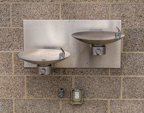 Two stainless steel drinking fountains on the side of a building in Frick Park, a city park in Pittsburgh, Pennsylvania, USA on a sunny spring day