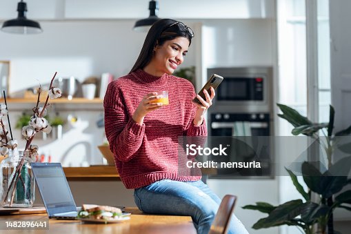 istock Beautiful young woman using smartphone while having healthy breakfast sitting on table at home 1482896441