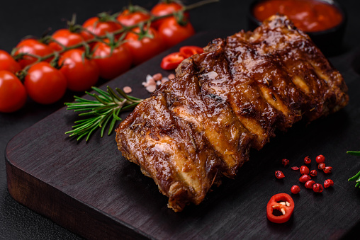 Delicious grilled pork ribs with sauce, spices and herbs on a dark concrete background