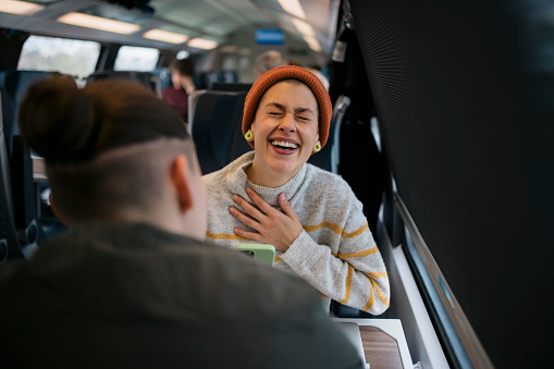 Young woman talking with her girlfriend and laughing sitting in train. Gay couple chatting while traveling by train.