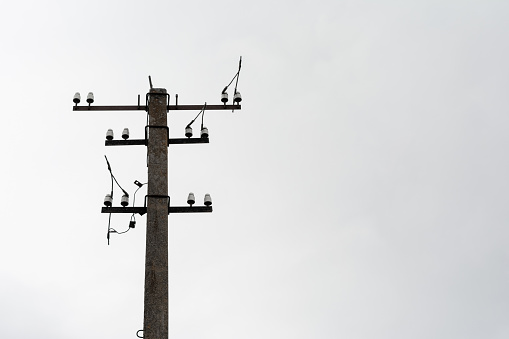 Ferroconcrete electrical pole with wires cut against a gloomy sky, view of the power line from below