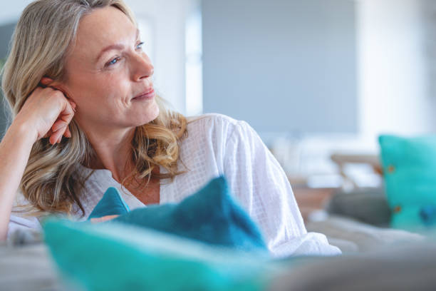 mature woman relaxing on the sofa. she looks contented and contemplative - menopause imagens e fotografias de stock