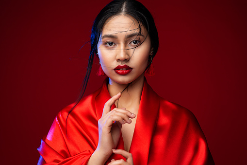 Beautiful Japanese Girl in Red Silk Kimono Dress. Asian Beauty Woman Face with Red Lips Makeup. Chinese Fashion Model showing Silence Sign. Fantasy Geisha Portrait
