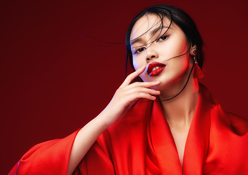 Beautiful Japanese Girl Face with Red Lips Makeup. Asian Beauty Woman in Red Silk Kimono Dress. Chinese Fashion Model. Fantasy Geisha Portrait