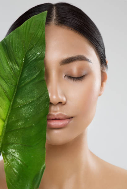 Skin Care. Natural Beauty Woman. Model with Fresh Clean Skin Make up and Full Lips with Big Green Tropic Leaf. Eco Cosmetics and Spa Cosmetology. Asian Girl Close up Portrait with Closed Eyes stock photo