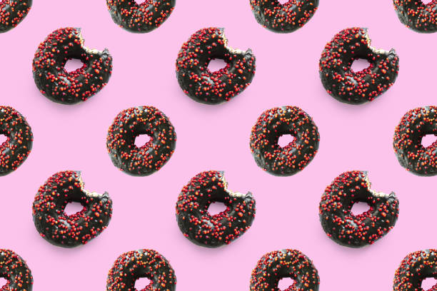 istock Black bited donuts with red glaze on pink background seamless pattern top view. Food dessert flatly flat lay of delicious sweet nibbles chocolate donuts 1482903138