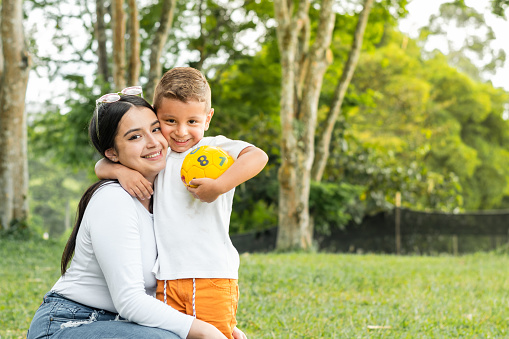 young mother with her son, playing with a ball in the park, girl hugging her little boy.