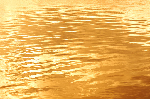 Water rippled surface background with gold yellow sunset light reflected