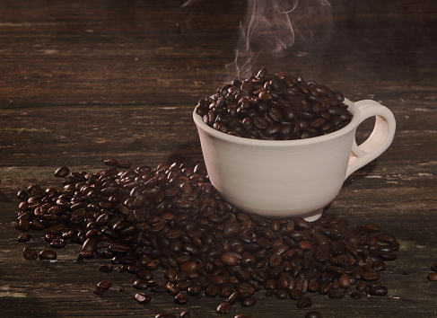 Coffee beans steaming in a white cup on a dark wood table