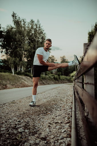 Athlete performing leg stretching exercises after a run in a natural environment. Fitness themed photograph showcasing physical activity flexibility and health