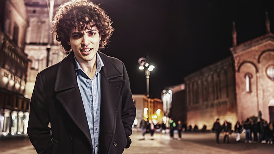 lone young man stands in the middle of the city streets at night, illuminated by the glow of the streetlights. The image evokes a sense of solitude and contemplation.
