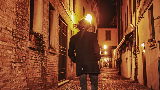 A young man walks alone in a dark alleyway in the city at night, embracing solitude.