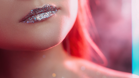 Glitter lips. Art makeup. Glamour visage. Cropped closeup of neon red color light woman face skin with sparkling metallic silver gloss on blur free space.