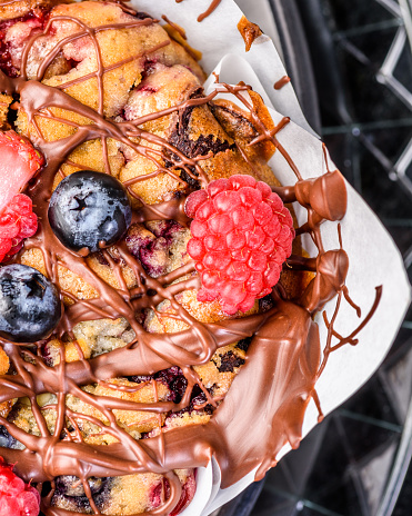 A close view of a muffin, covered with chocolate icing, strawberries and blueberries