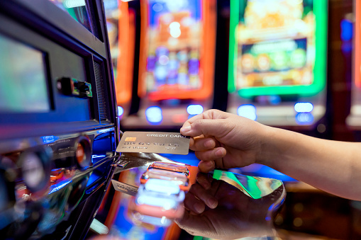 Slot Machine gambling bet Play Time. Female Gambler Hand hold credit card ready to win the game with one best shot casino close up female Hand holding credit card playing slot machine gambling closeup