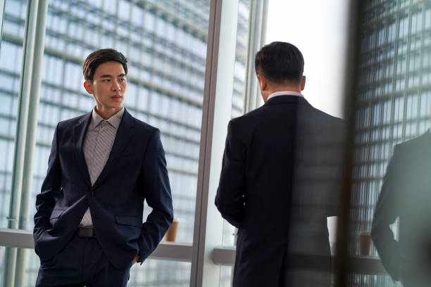 istock two asian businesspeople talking chatting standing by the window talking chatting in office 1482966318