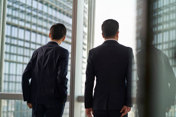 istock two asian businesspeople talking chatting standing by the window talking chatting in office 1482966319