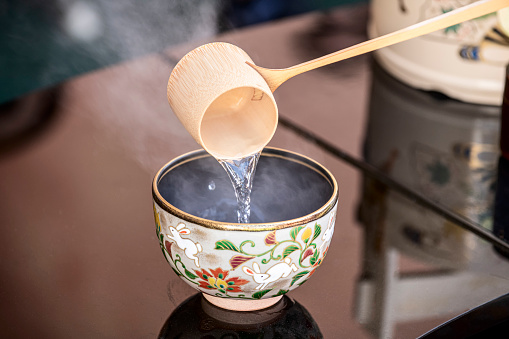Pouring hot water during a Japanese tea ceremony with reflected  table surface in the background.