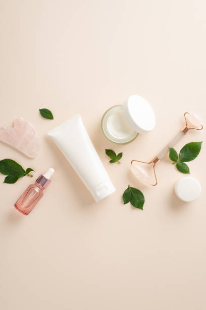 istock Elevate your self-care routine with top view vertical cosmetology concept featuring pump bottles of face roller serum and cream, massage rollers, and green leaves on a serene pastel beige backdrop 1482978793