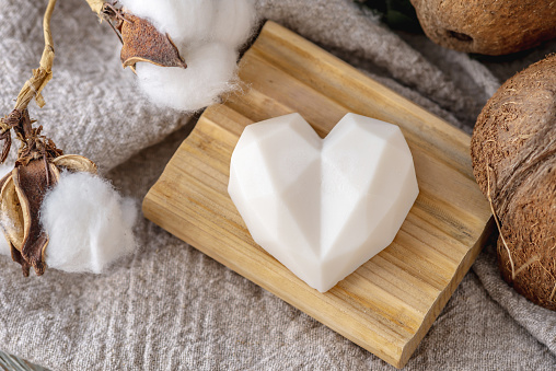 Piece of cute white natural soap in the shape of a heart on the wooden soap dish.