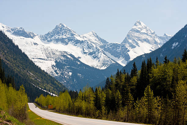 Rogers Pass Highway through the Rogers Pass in the Canadian Rockies against a backdrop of forested hillsides and snow-capped mountain peaks. yoho national park photos stock pictures, royalty-free photos & images