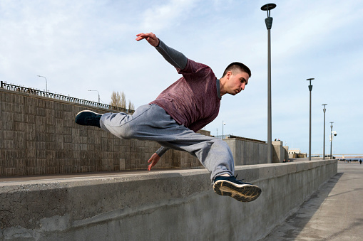 Sports man doing parkour. Parkour athlete training in city in sportive clothes. Free runner jumping have workout at daytime.