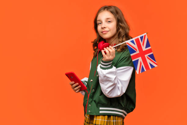 Girl holds small UK flag Teen girl in school outfit and red headphones holds cellphone and small UK flag. Concept of Studying in United Kingdom of Great Britain. english culture stock pictures, royalty-free photos & images