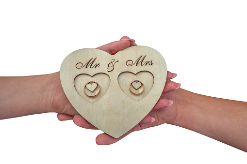 Hands of the bride and groom, rings on a wooden stand in the form of a heart. Mr and Mrs sign. Isolated on white