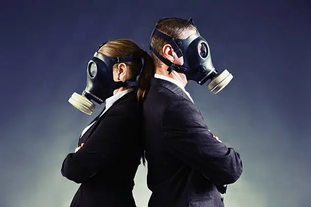 A formally-dressed couple wearing gas masks stand back to back. Could be a disagreement or a simple odor issue! 
