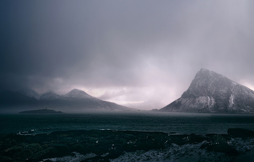 Snowcapped mountains with Norwegian sea during foggy winter day in Lofoten.