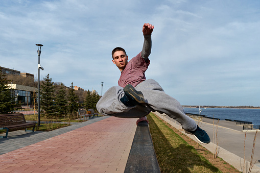 Sport man practicing parkour in urban space. Parkour athlete in sportswear jumping over the railing. Free runner have workout city street.