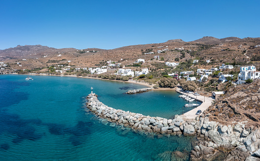 Tinos island, Cyclades Greece. Aerial drone view of Agios Romanos village, transparent blue sea, rocky breakwater, bay, moored boat at port.