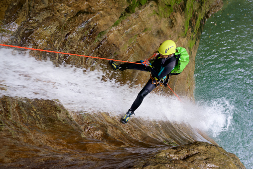 Extreme canyoning series. Male explorer rappeling down the waterfall deep in the mountains.