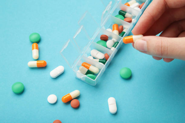 istock Female hand sorting pills in pillbox on blue background 1482998229