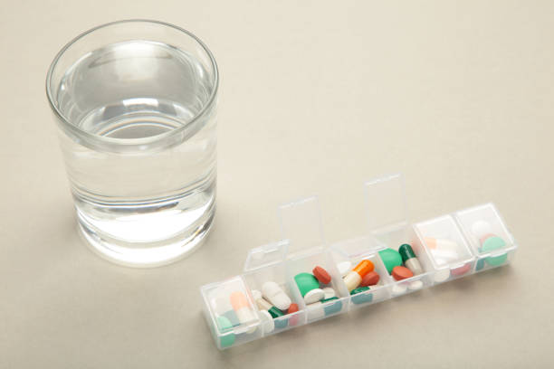 istock Pill box with medicaments and glass of water on grey background. Space for text 1482998304