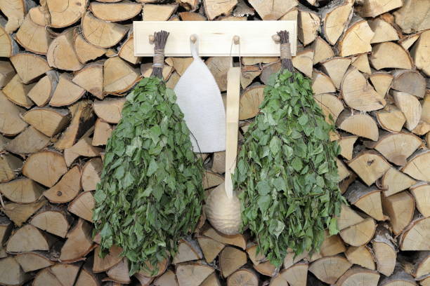 A couple of dry birch brooms, ladle and hat for a  sauna and bath treatments are hanging a on woodpile of chopped birch firewood.