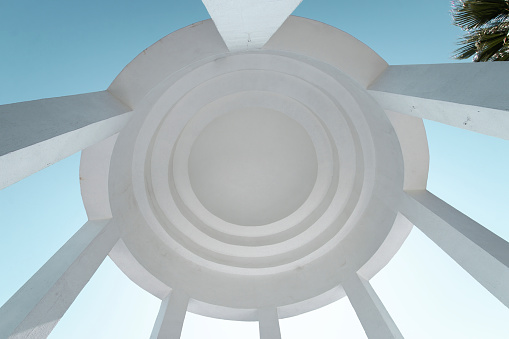Low angle view inside dome of a white rotunda with architectural coloumns against blue sky