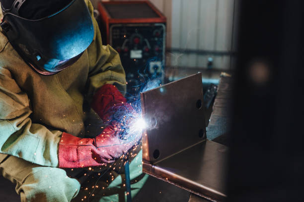 Welding concept. Industrial worker or welder wears protective mask and gloves erects technical steel on factory. Labour worker welds metal. Man repairs detail in cars auto service. Steel worker