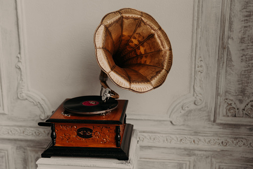 Old gramophone with horn speaker stands against anicent background, produces songs recorded on plate. Music and nostalgia concept. Gramophone with phonograph record