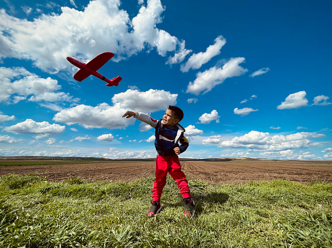 Against a stunning blue sky dotted with clouds, a small child gleefully runs around with his toy plane. The scene is one of carefree joy, with the vast expanse of sky providing a sense of boundlessness and freedom