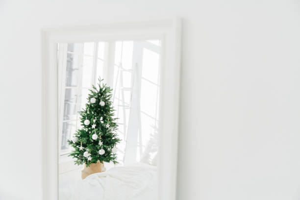 istock Decorated Christmas tree reflecting in mirror, white spacious room. Bedroom with New Year decoration. Modern classic style. Christmas eve at home 1483003566