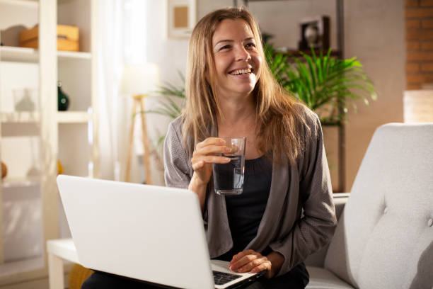 istock Smiling girl drinking water while using the laptop. 1483005866