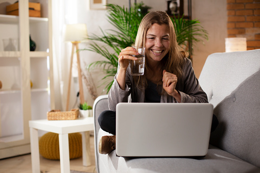 Girl holding a glass of water. Smiling girl drinking water while using the laptop