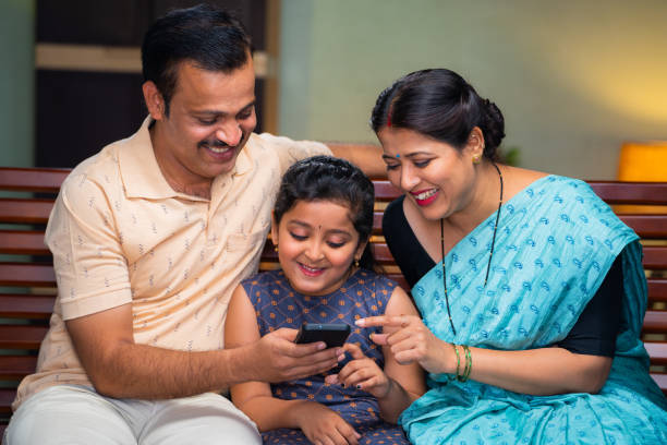 istock Happy smiling couple with daughter watching mobile phone while sitting on sofa at home - concept of family time, cyberspace and caring parents 1483006012