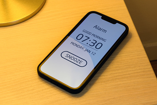 Smartphone alarm clock on bedroom night table with snooze button, selective focus