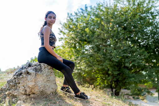 A teenage girl wearing a bustier and leggings is walking in the mountains.