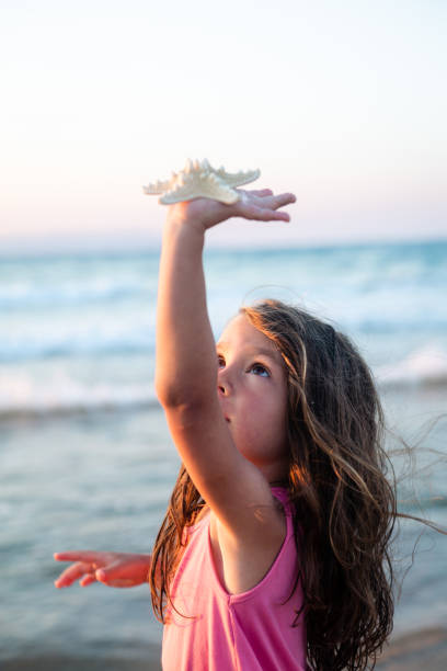 Curious little girl explore the sea world , looking at and playing with starfish