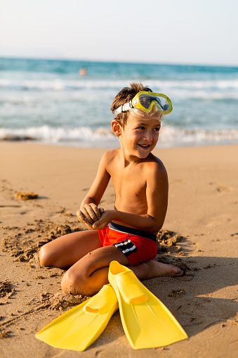 Little boy with scuba gear sitting on the beach