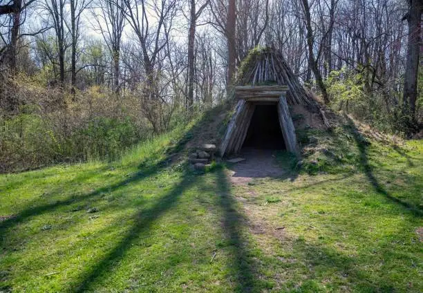 Collier's hut one-person shelter made out of wooden poles and mud sod exterior. Enchanted shaman sweat lodge concept in idyllic nature background. Beautiful nature setting with long shadows for magical feeling.
