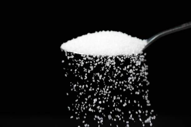 istock Macro photography of a teaspoon with white sugar on a black background, copy space. White sugar is poured from a teaspoon. 1483016895
